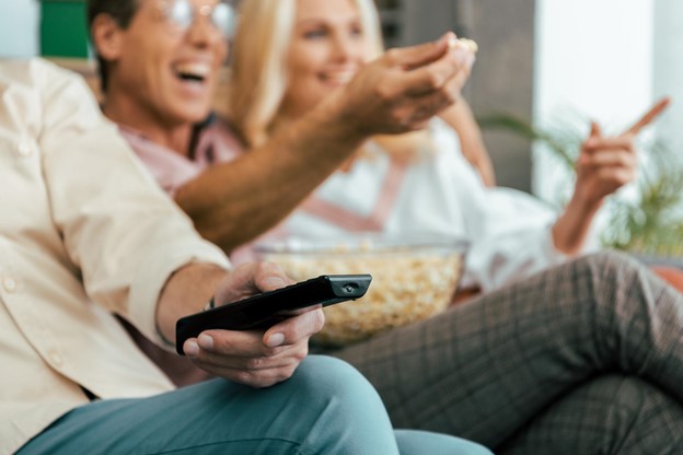 People eating popcorn and laughing at TV.