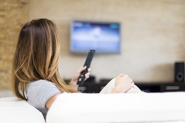 Woman sitting on couch watching TV and using a TV remote