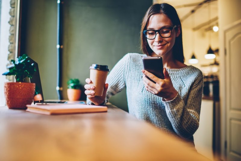 woman drinking coffee and reading on her phone