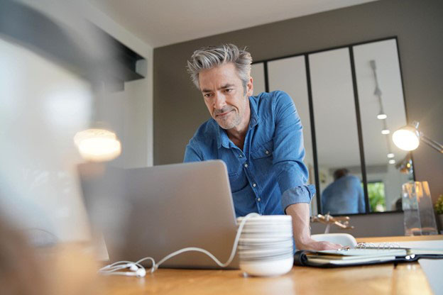 man in an office standing at desk look at laptop